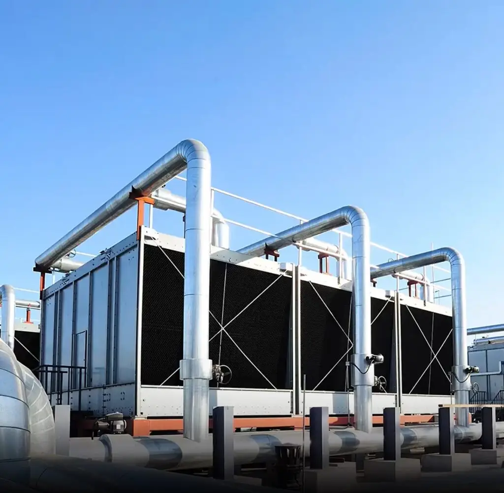A imagem mostra grandes torres de resfriamento industrial com tubulações metálicas ao ar livre, sob um céu azul. Essas torres retangulares, que fazem parte do sistema de resfriamento, possuem painéis pretos com aberturas e estão interligadas por tubos prateados, compondo o cenário típico das soluções industriais Tecnogera.