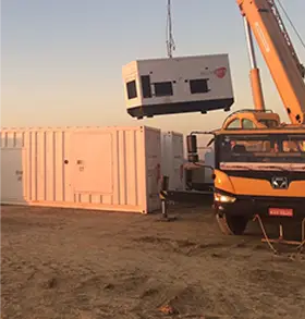 Um caminhão guindaste amarelo da Tecnogera levanta um grande gerador industrial branco-possivelmente usado para energia de biomassa-sobre um terreno arenoso em um canteiro de obras. Ao fundo, há outros contêineres e o pôr do sol ilumina a cena, destacando o trabalho dessa produtora independente.