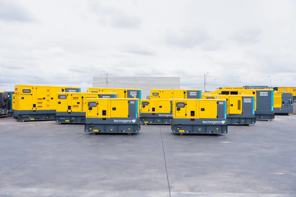 Vários geradores amarelos da Tecnogera estão alinhados para garantir energia contínua em setores que não podem parar, mesmo em dias nublados