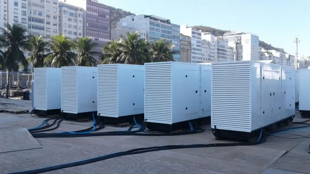 Os geradores da Tecnogera estão alinhados em uma área externa sobre painéis de madeira, prontos para fornecer energia para o evento