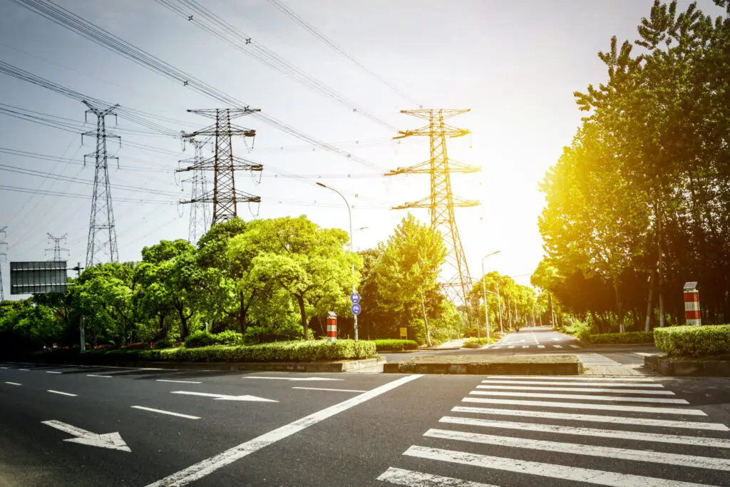 Um cruzamento tranquilo, emoldurado por vegetação e altos postes de eletricidade, destaca a geração de energia elétrica.