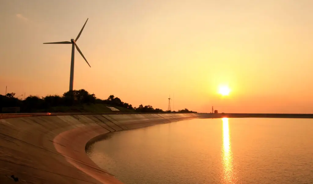 O pôr do sol ilumina turbinas de vento perto de um reservatório, demonstrando a matriz energética.